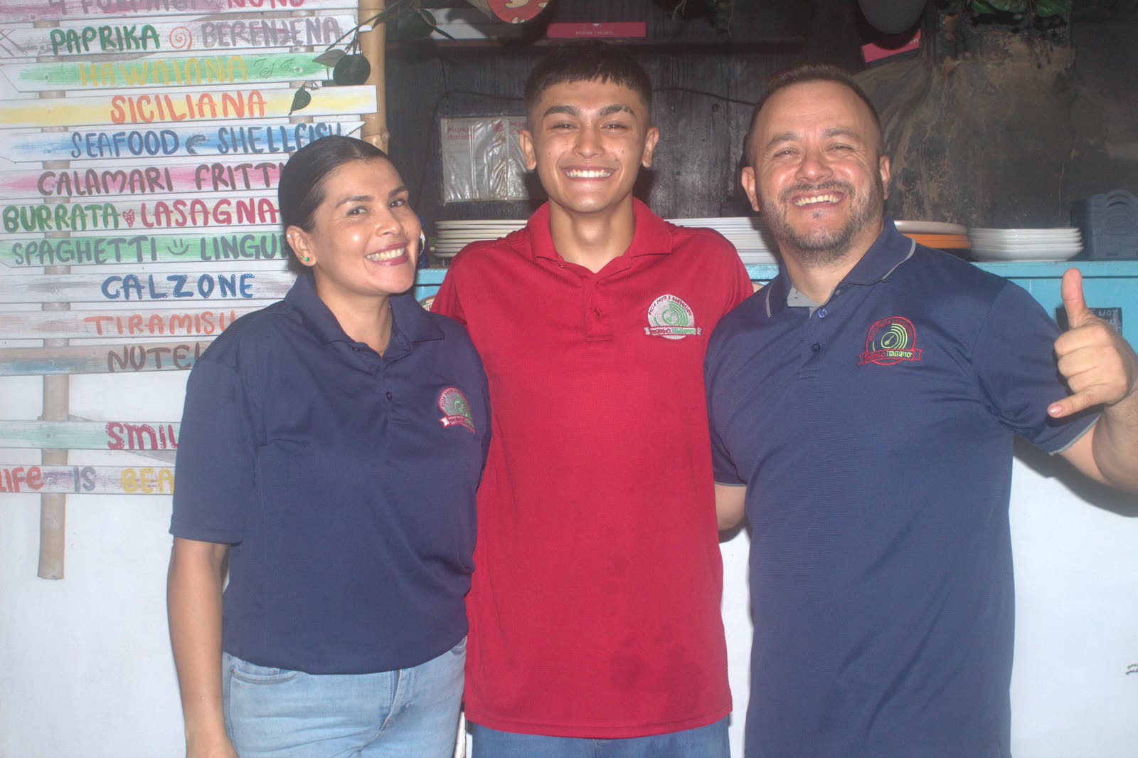 La familia dueña de Mambo Italiano sonriendo juntos frente a la pizarra del menú